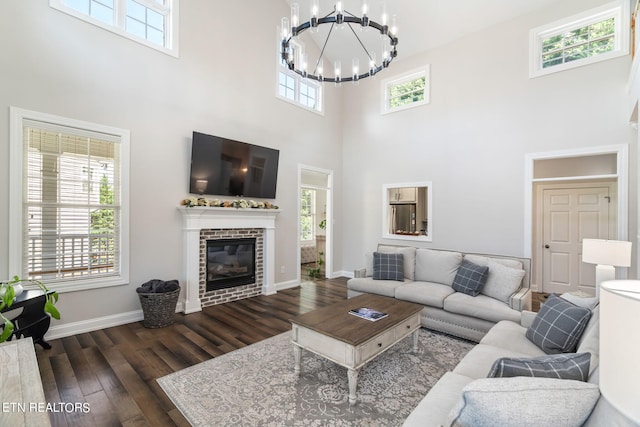 living room featuring a fireplace, a towering ceiling, dark wood-type flooring, and a notable chandelier