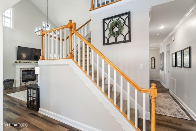 staircase featuring a notable chandelier, wood-type flooring, ornamental molding, and a brick fireplace