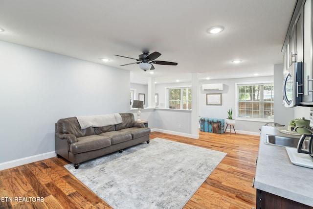 living room featuring an AC wall unit, light hardwood / wood-style flooring, sink, and ceiling fan