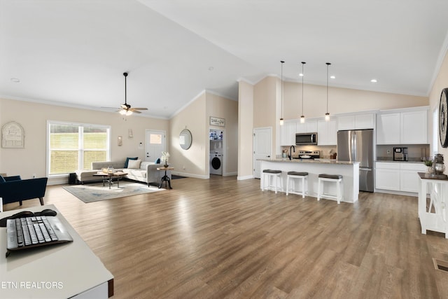 kitchen featuring washer / clothes dryer, an island with sink, white cabinetry, stainless steel appliances, and decorative light fixtures