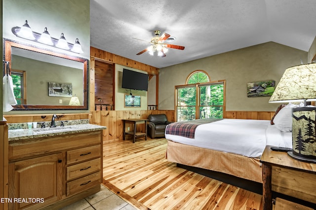 bedroom with light hardwood / wood-style flooring, wooden walls, a textured ceiling, and sink