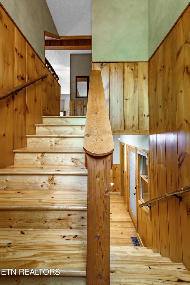 staircase featuring hardwood / wood-style flooring, wood walls, vaulted ceiling, and a textured ceiling