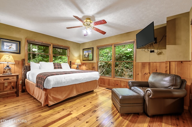 bedroom featuring a textured ceiling, light hardwood / wood-style floors, wooden walls, and ceiling fan