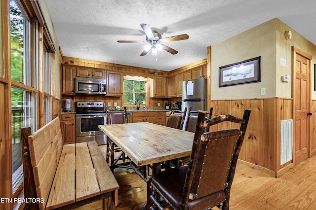 dining space with wood walls, light wood-type flooring, a textured ceiling, ceiling fan, and sink