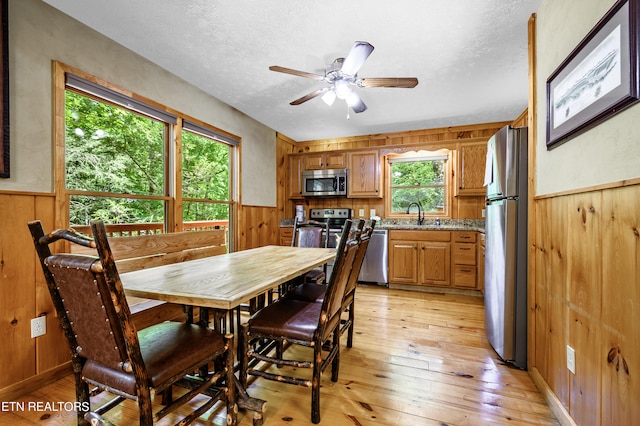 dining area featuring ceiling fan, wooden walls, light hardwood / wood-style flooring, and a textured ceiling