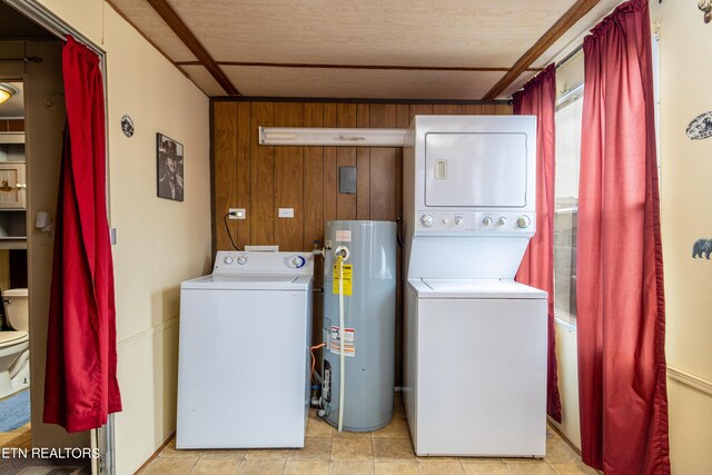 clothes washing area featuring gas water heater, wood walls, light tile patterned floors, and stacked washer and dryer