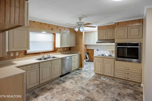 kitchen with ceiling fan, appliances with stainless steel finishes, sink, and wooden walls