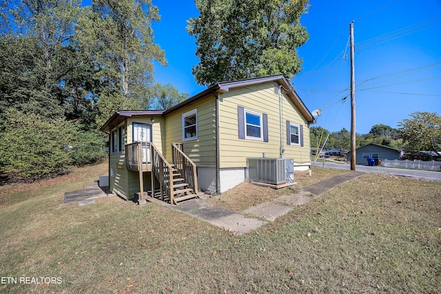 rear view of house with central air condition unit and a lawn