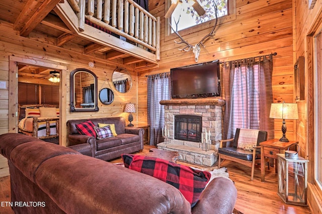 living room with a fireplace, beamed ceiling, ceiling fan, hardwood / wood-style flooring, and wooden walls