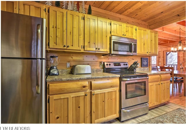 kitchen with hanging light fixtures, wood walls, appliances with stainless steel finishes, wooden ceiling, and light wood-type flooring