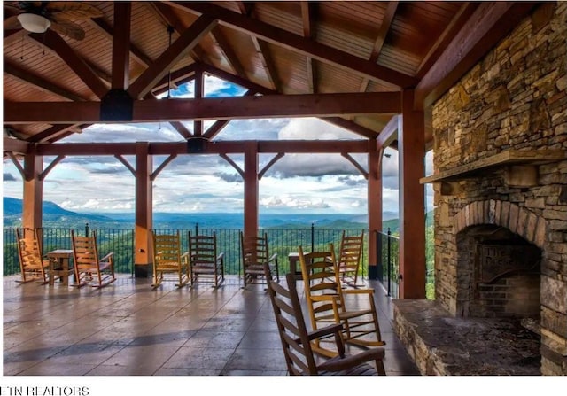 view of patio featuring a water and mountain view, a gazebo, ceiling fan, and an outdoor stone fireplace