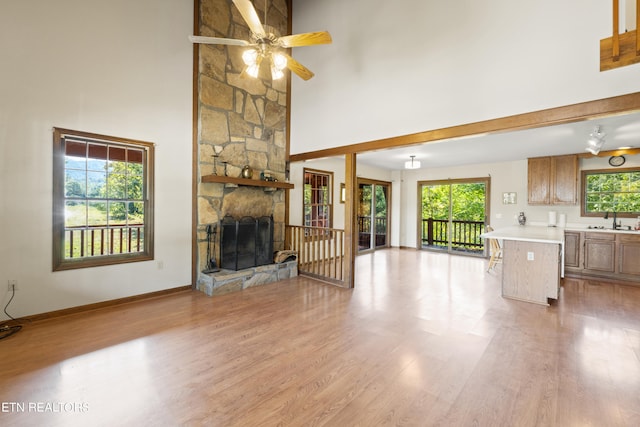 unfurnished living room featuring a high ceiling, a stone fireplace, ceiling fan, and plenty of natural light