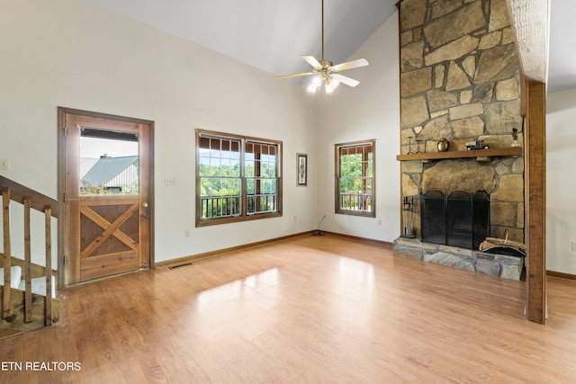 unfurnished living room with high vaulted ceiling, light wood-type flooring, ceiling fan, and a stone fireplace