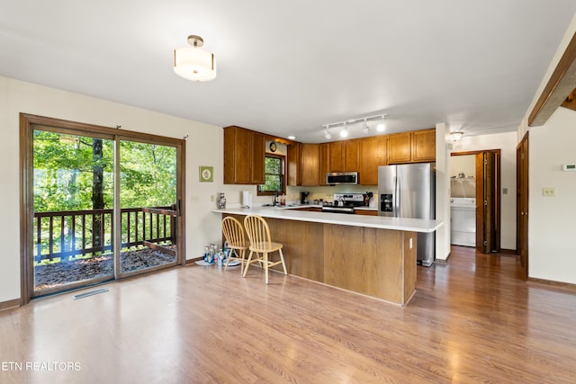 kitchen featuring sink, kitchen peninsula, light hardwood / wood-style flooring, track lighting, and appliances with stainless steel finishes