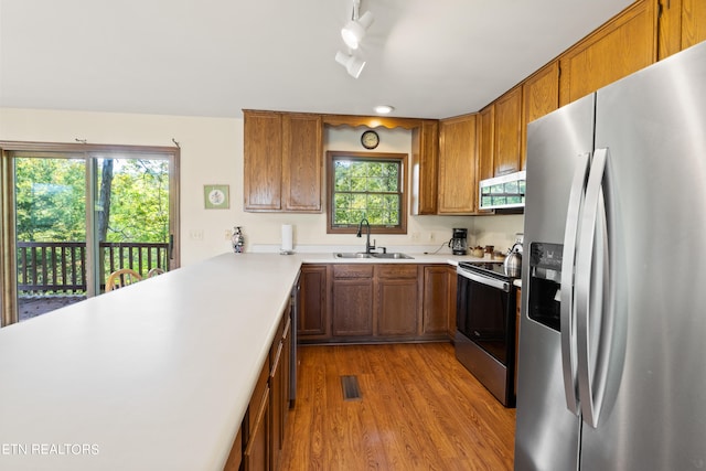 kitchen with appliances with stainless steel finishes, rail lighting, kitchen peninsula, light hardwood / wood-style flooring, and sink