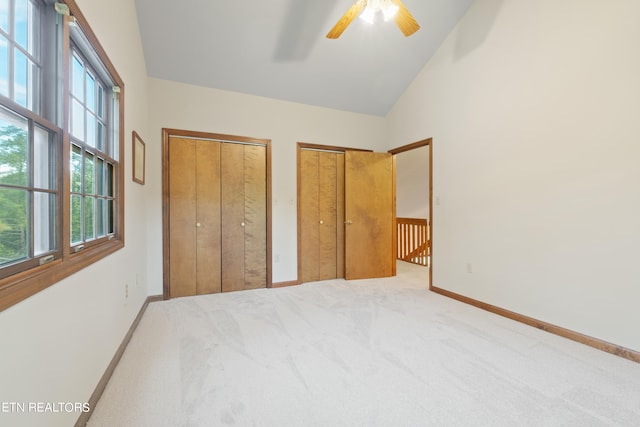 unfurnished bedroom with ceiling fan, carpet floors, two closets, and high vaulted ceiling