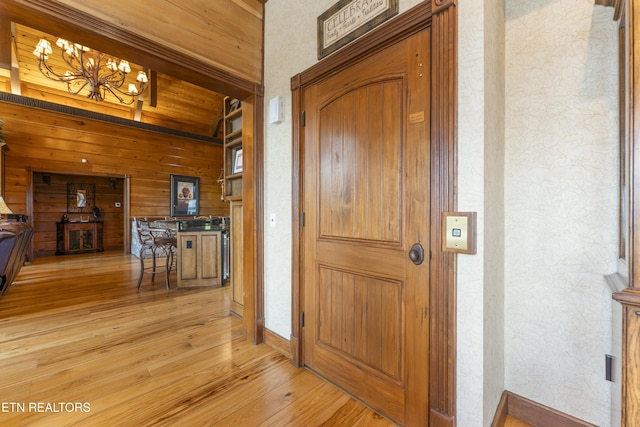 hall with wood walls, light hardwood / wood-style floors, and a notable chandelier