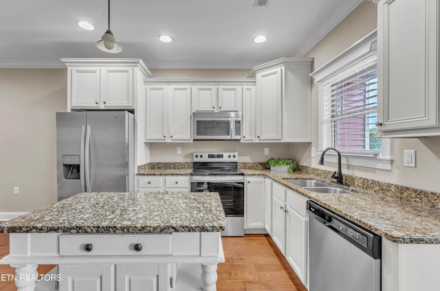 kitchen with appliances with stainless steel finishes, white cabinetry, a kitchen island, light hardwood / wood-style flooring, and sink