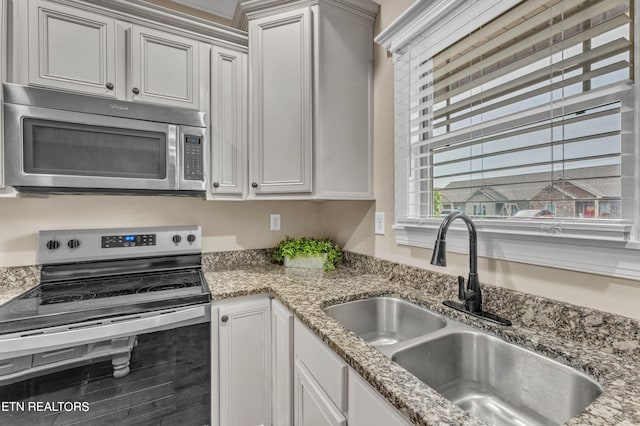 kitchen with appliances with stainless steel finishes, white cabinetry, light stone counters, wood-type flooring, and sink