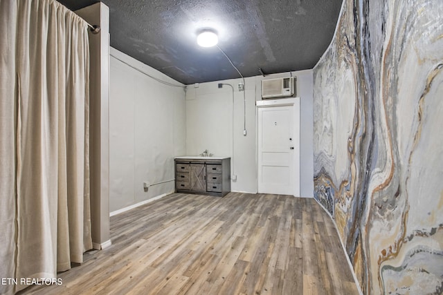 basement featuring a textured ceiling, light hardwood / wood-style floors, and an AC wall unit