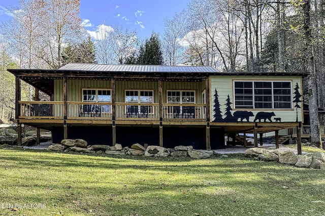 rear view of property featuring board and batten siding, metal roof, a lawn, and a wooden deck