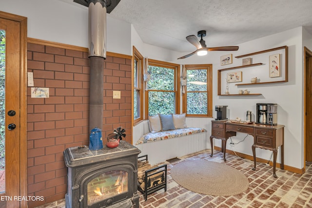 sitting room with ceiling fan, a textured ceiling, and a wood stove