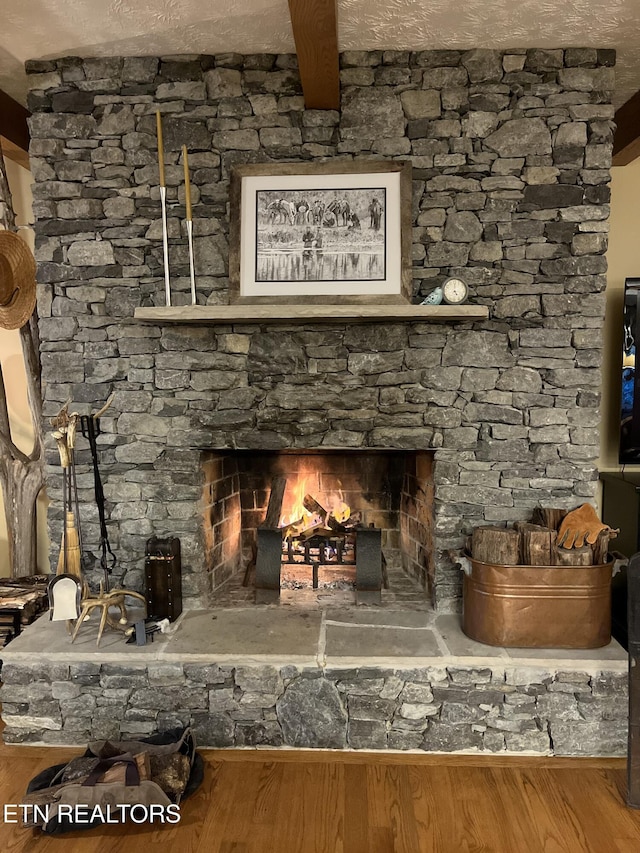 interior details featuring beamed ceiling, wood-type flooring, a stone fireplace, and a textured ceiling