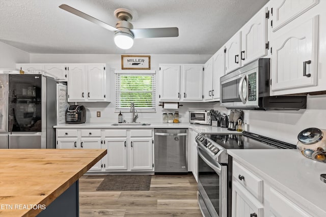 kitchen featuring white cabinets, stainless steel appliances, light hardwood / wood-style flooring, ceiling fan, and sink