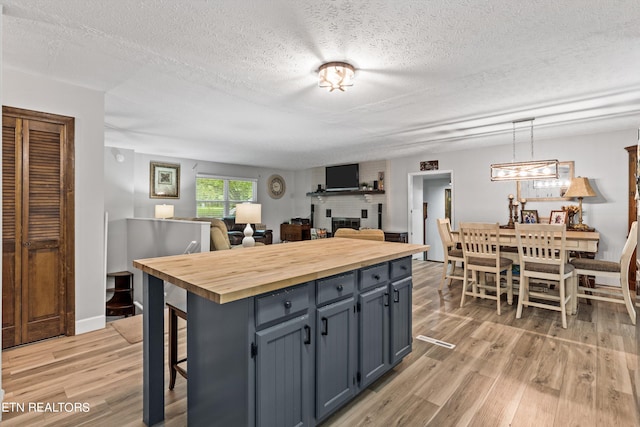 kitchen featuring light hardwood / wood-style floors, a textured ceiling, a brick fireplace, decorative light fixtures, and butcher block countertops