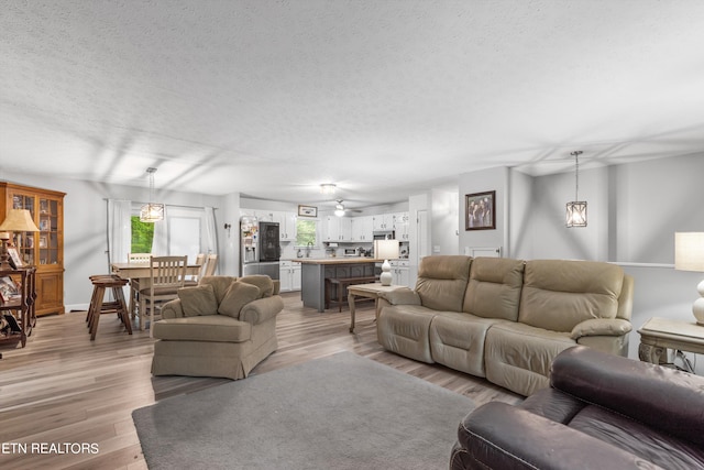 living room with ceiling fan, a textured ceiling, and light hardwood / wood-style flooring