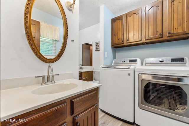 clothes washing area with a textured ceiling, light wood-type flooring, sink, and washing machine and clothes dryer