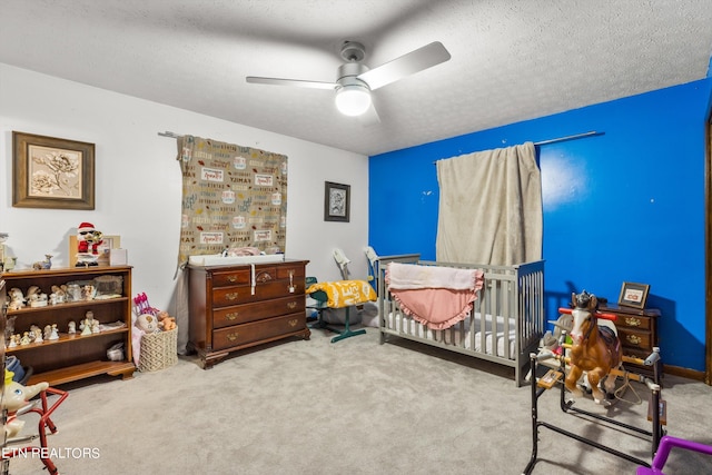 carpeted bedroom featuring a textured ceiling, ceiling fan, and a nursery area