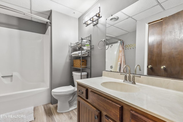 full bathroom with wood-type flooring, a drop ceiling, shower / tub combo with curtain, vanity, and toilet