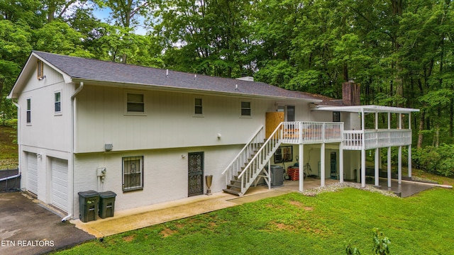 rear view of house featuring a garage, a wooden deck, a lawn, and a patio area