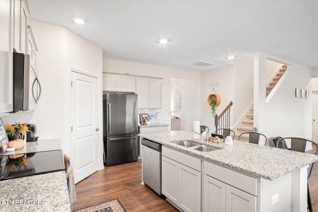 kitchen featuring light stone counters, a kitchen island with sink, sink, a kitchen bar, and appliances with stainless steel finishes