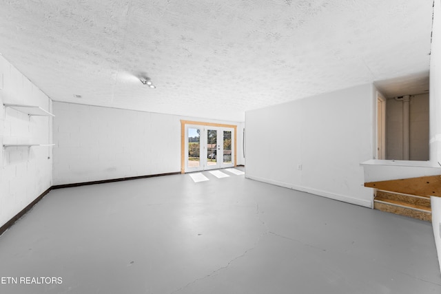 spare room with concrete floors, french doors, concrete block wall, and a textured ceiling
