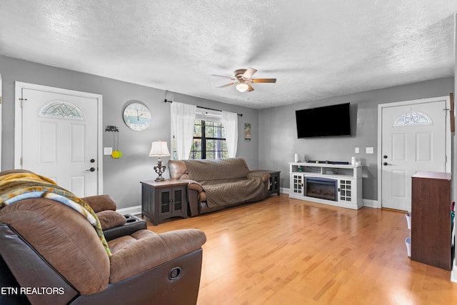 living room with ceiling fan, light wood-type flooring, and a textured ceiling