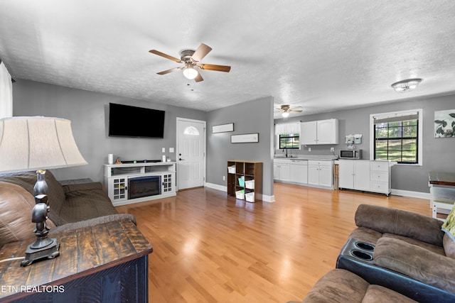 living room featuring a fireplace, light wood-type flooring, ceiling fan, and a textured ceiling