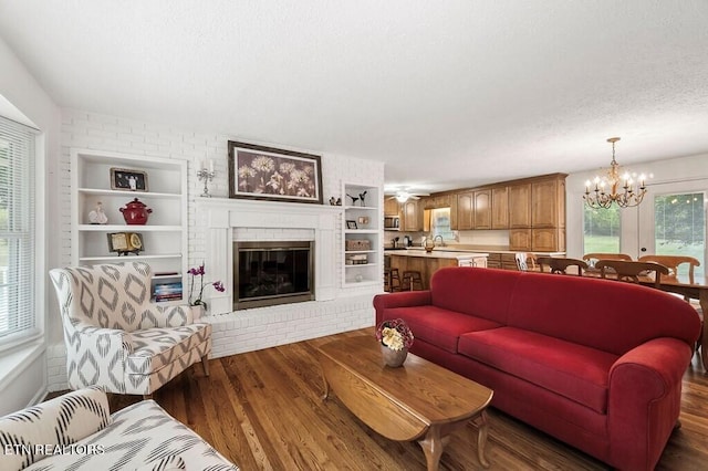 living room featuring a textured ceiling, dark hardwood / wood-style floors, sink, a notable chandelier, and a brick fireplace