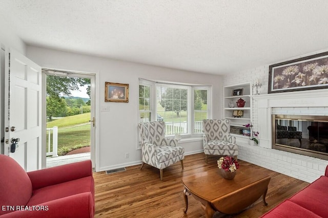 living room with a brick fireplace, a textured ceiling, and hardwood / wood-style flooring