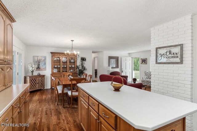 kitchen with a textured ceiling, decorative light fixtures, dark wood-type flooring, a center island, and an inviting chandelier