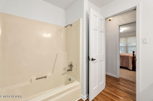 bathroom featuring hardwood / wood-style floors, a textured ceiling, and washtub / shower combination