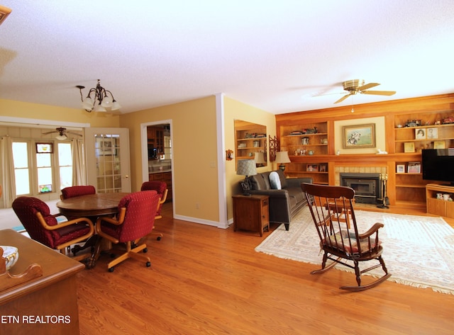 dining room featuring built in shelves, a textured ceiling, ceiling fan with notable chandelier, and light wood-type flooring