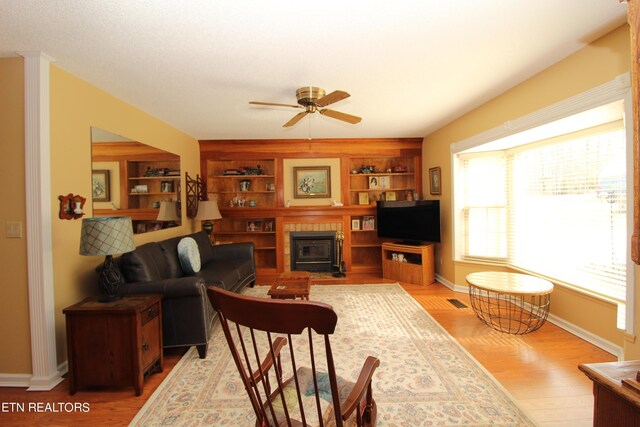 living room with built in shelves, ceiling fan, and light hardwood / wood-style flooring