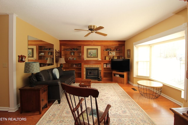 living room featuring baseboards, light wood-type flooring, a tiled fireplace, and a ceiling fan