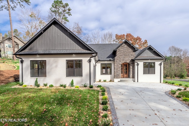 modern farmhouse with stone siding, a front lawn, board and batten siding, and brick siding