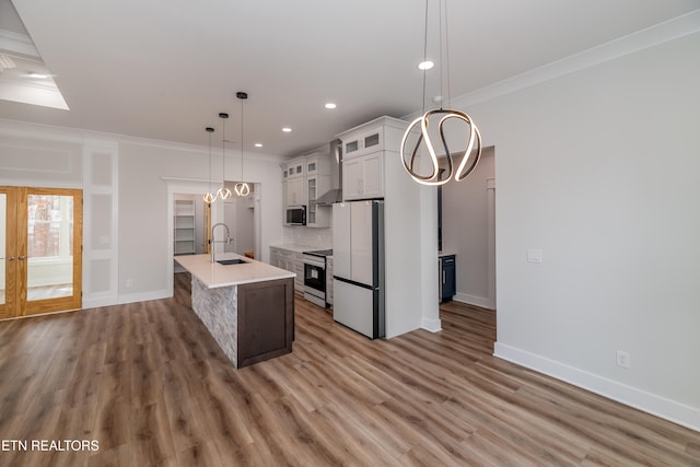 kitchen featuring stainless steel appliances, light countertops, ornamental molding, a sink, and wall chimney exhaust hood