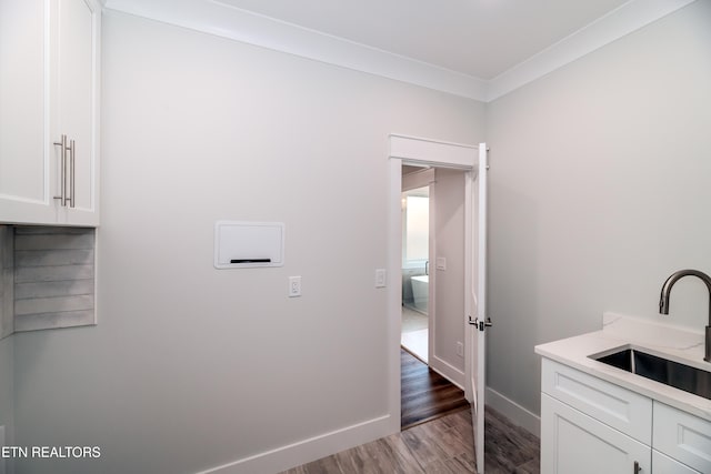 laundry area with crown molding, wood finished floors, a sink, and baseboards