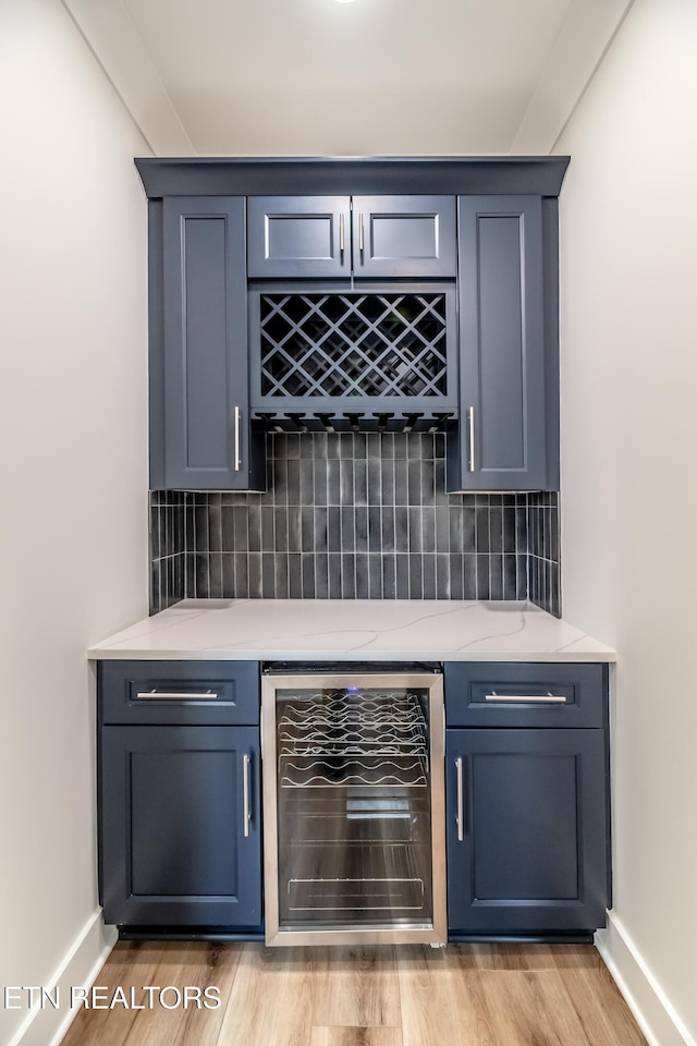 bar with decorative backsplash, beverage cooler, light wood-style floors, and a bar