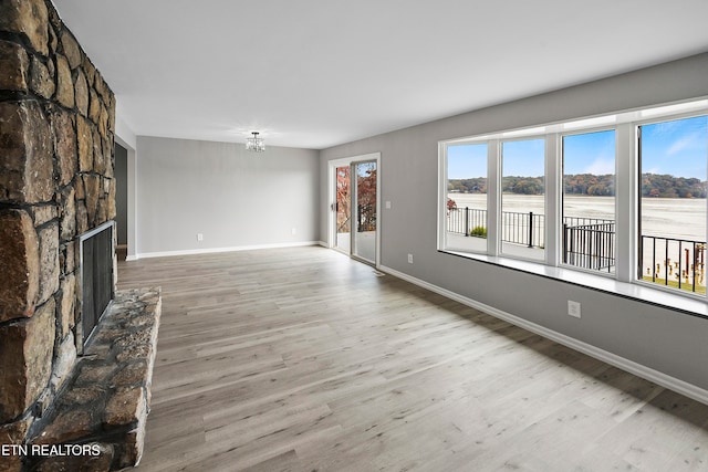 unfurnished living room featuring a stone fireplace, a water view, and light wood-type flooring